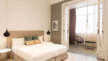 Habitación de hotel con una cama grande, una mesita redonda pequeña, una silla y una puerta que da a un balcón.
