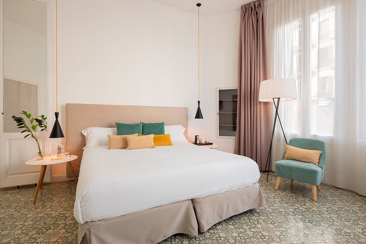 A hotel room with a large bed, a bedside table, a lamp, a chair, and a window with curtains.