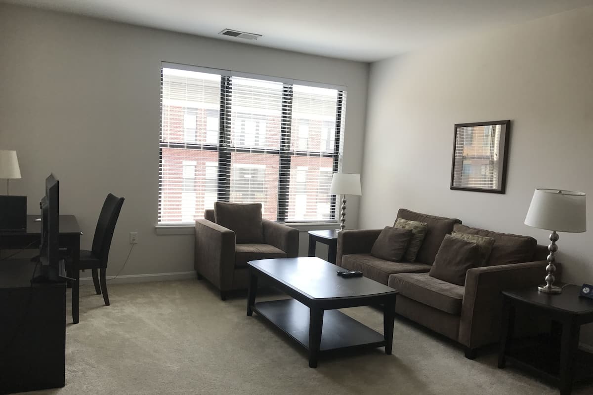 A living room with a sofa, armchair, coffee table, and a TV on a stand.