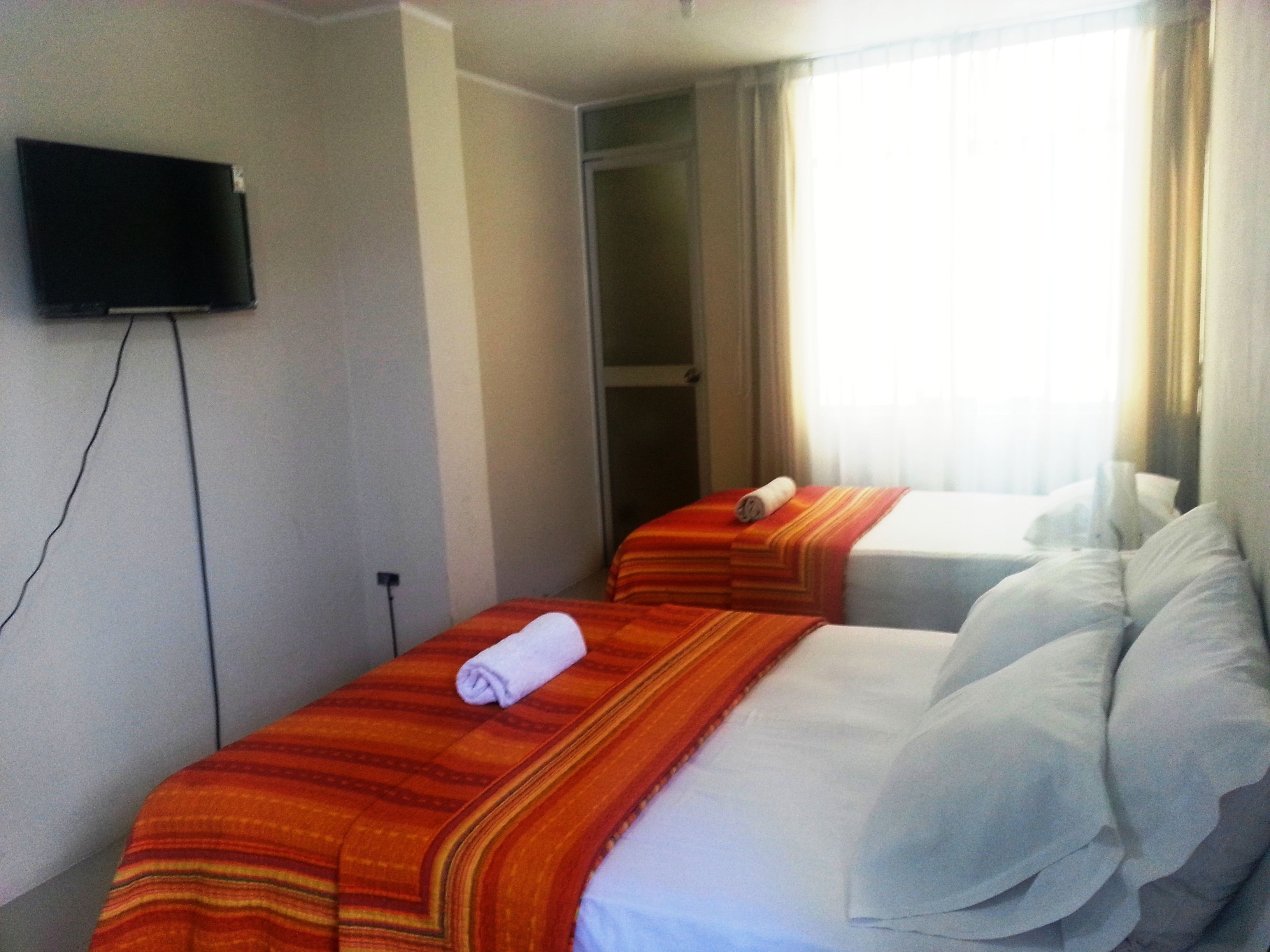 Ein Hotelzimmer mit zwei Betten, einem an der Wand befestigten Fernseher und einem Fenster mit Vorhängen.