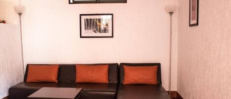 A modern living room with a black leather sofa, orange cushions, a small wooden coffee table, and two floor lamps.