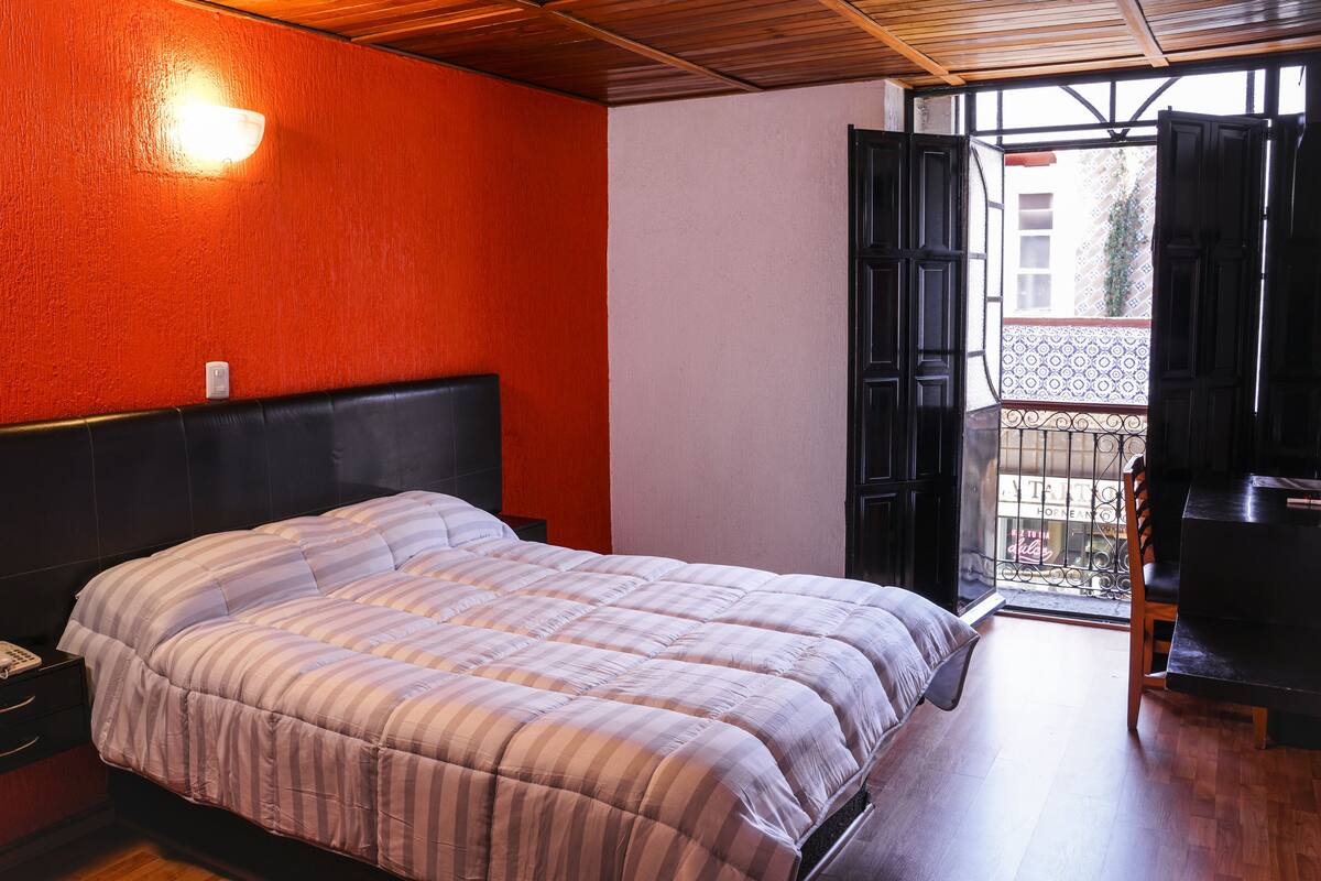 Un dormitorio con cama, mesita de noche, lámpara de pared y puerta abierta a un balcón.