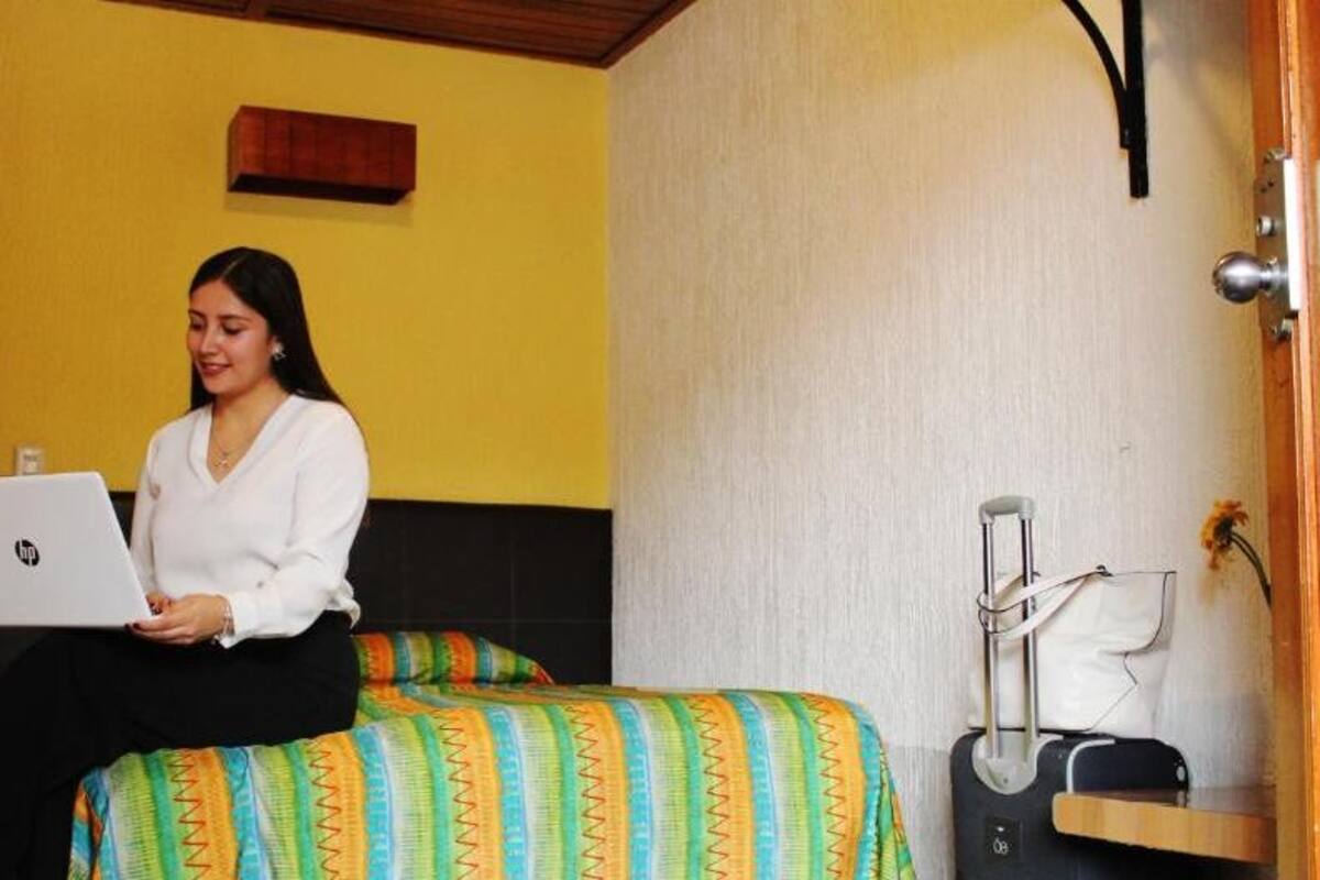 Una habitación con una cama, una maleta y un ordenador portátil.