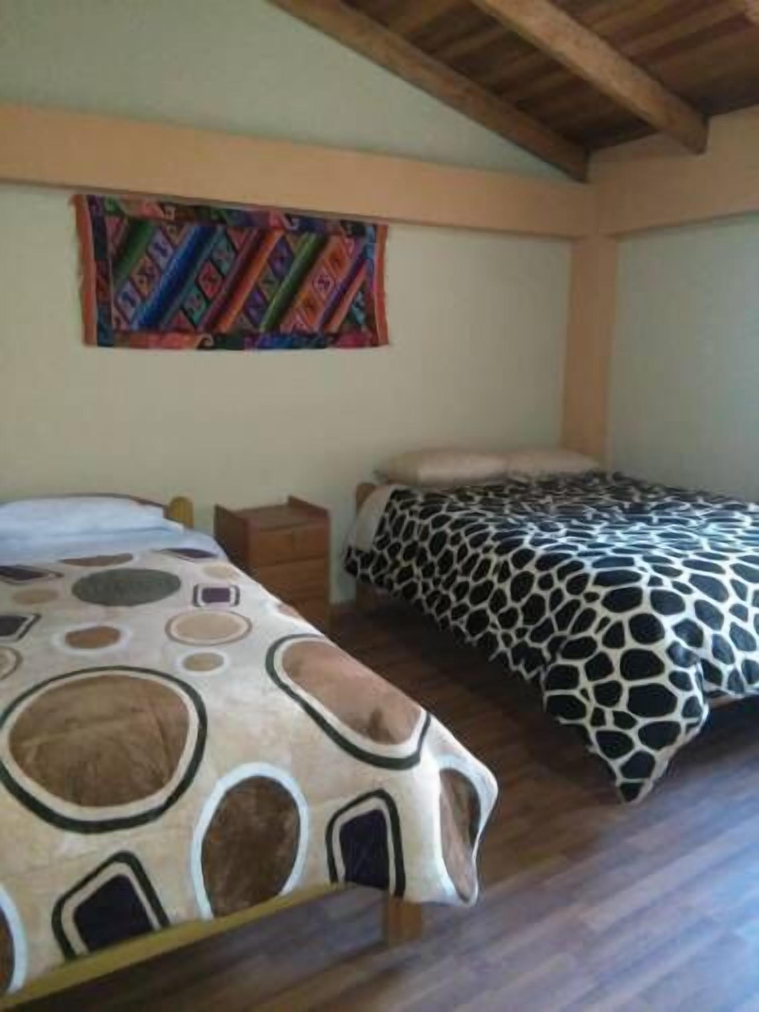 Une chambre avec deux lits, chacun recouvert d’une courtepointe à motifs différents. Une tapisserie colorée est accrochée au mur, au-dessus des lits.
