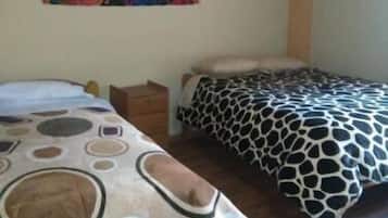 Une chambre avec deux lits, chacun recouvert d’une courtepointe à motifs différents. Une tapisserie colorée est accrochée au mur, au-dessus des lits.