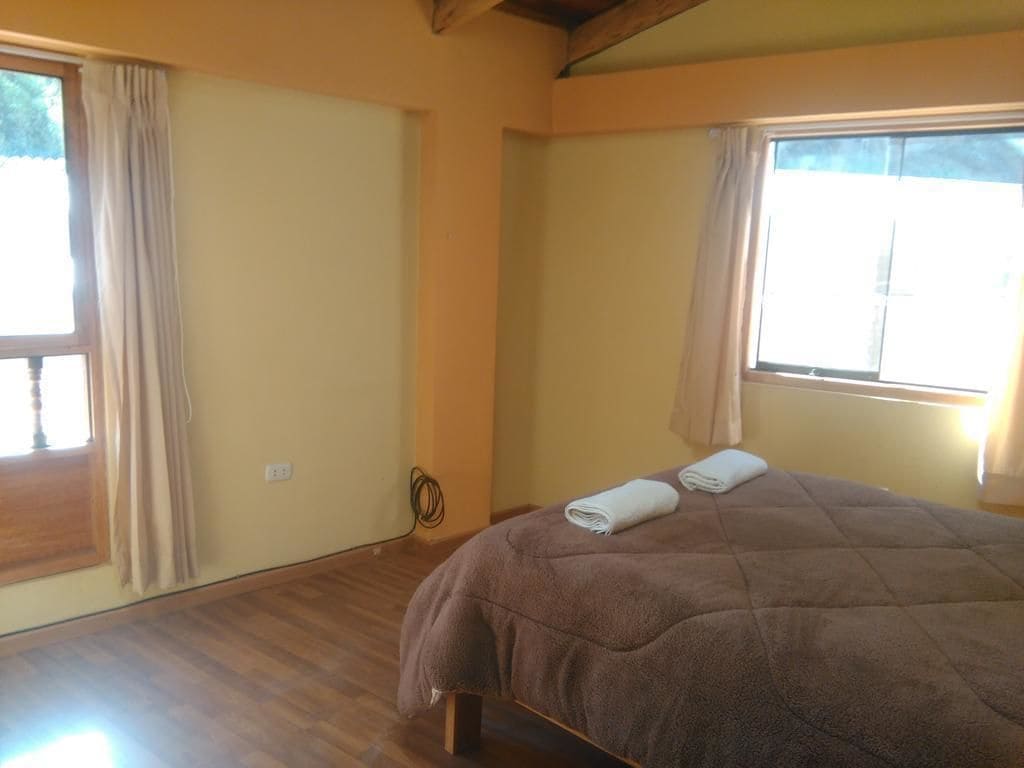 A bedroom with a bed, wooden flooring, and large windows with curtains.