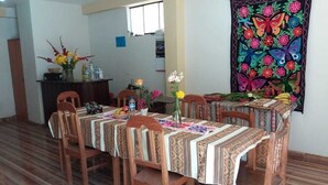 A dining area with a long table, chairs, and a decorative tapestry on the wall.