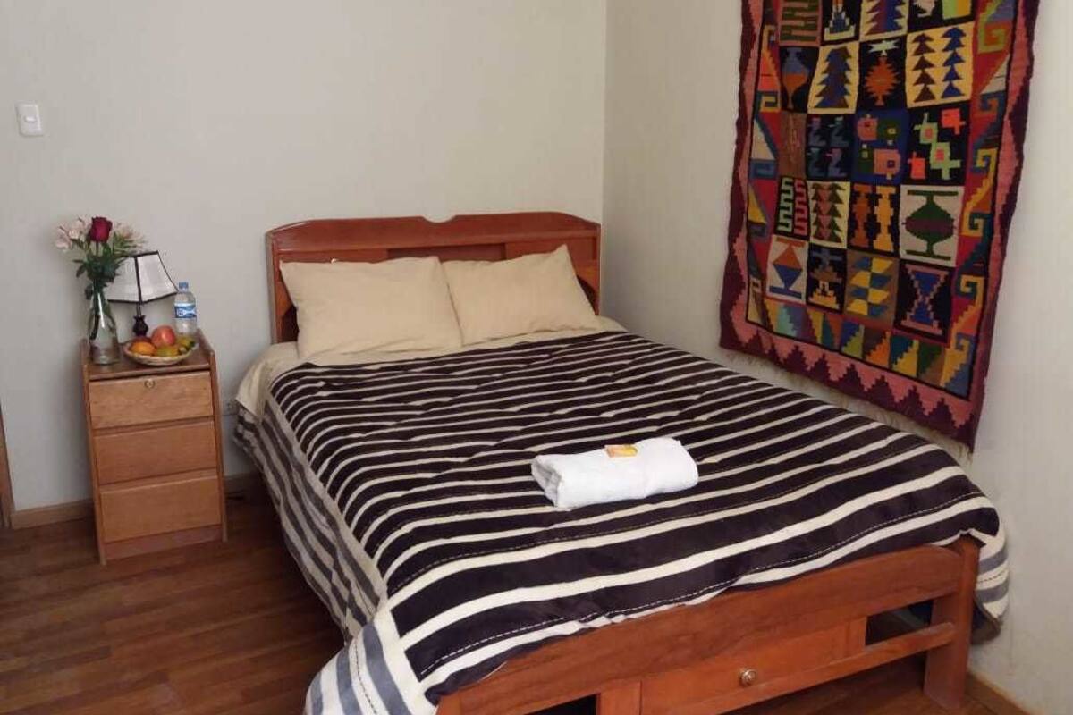 A bed with a striped bedspread, a wooden headboard, and a colorful tapestry on the wall.