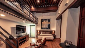 A modern hotel room with a wooden ceiling, a large bed, a TV, a seating area with a sofa and chairs, and a staircase. - Domingo Santo Hotel Boutique - Adults Only (Mexico City)