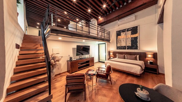 A modern loft-style bedroom with a loft bed, a wooden staircase, a flat-screen TV, a desk, and a comfortable seating area. - Domingo Santo Hotel Boutique - Adults Only (Mexico City)