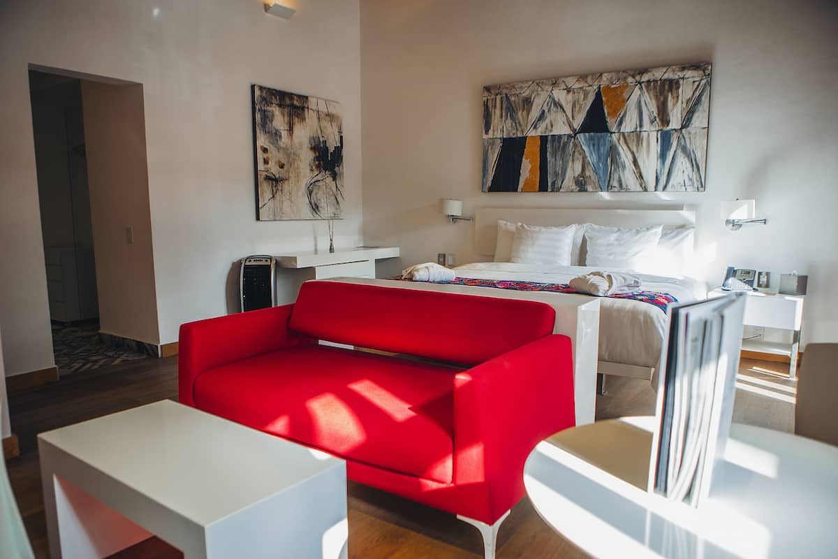 Ein modernes Hotelzimmer mit einem roten Sofa, einem weißen Bett und abstrakter Kunst an den Wänden.