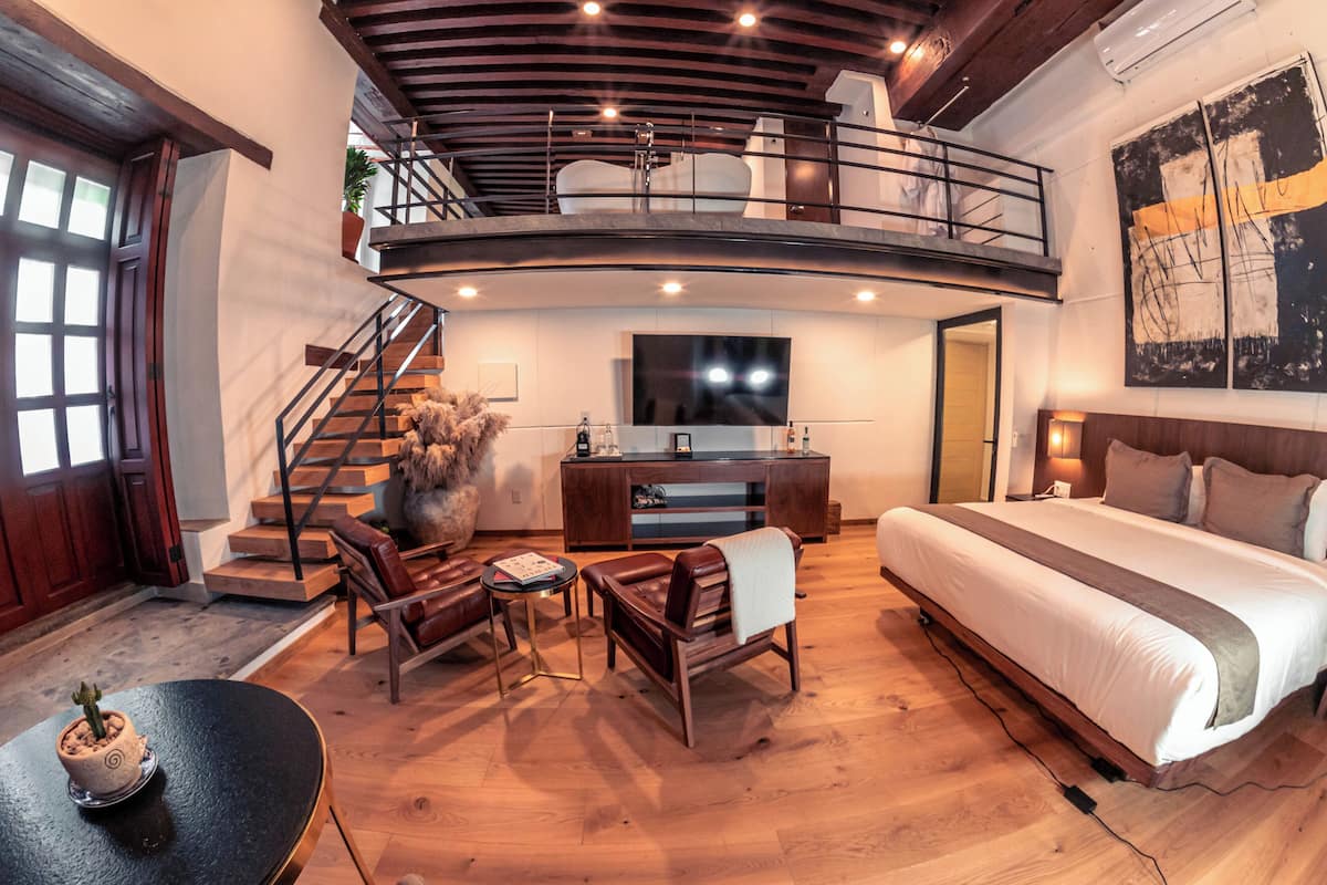 Ein geräumiges Schlafzimmer mit einem großen Bett, einem Schreibtisch und einem Stuhl. Eine Treppe führt zu einer oberen Ebene mit einem Balkon.