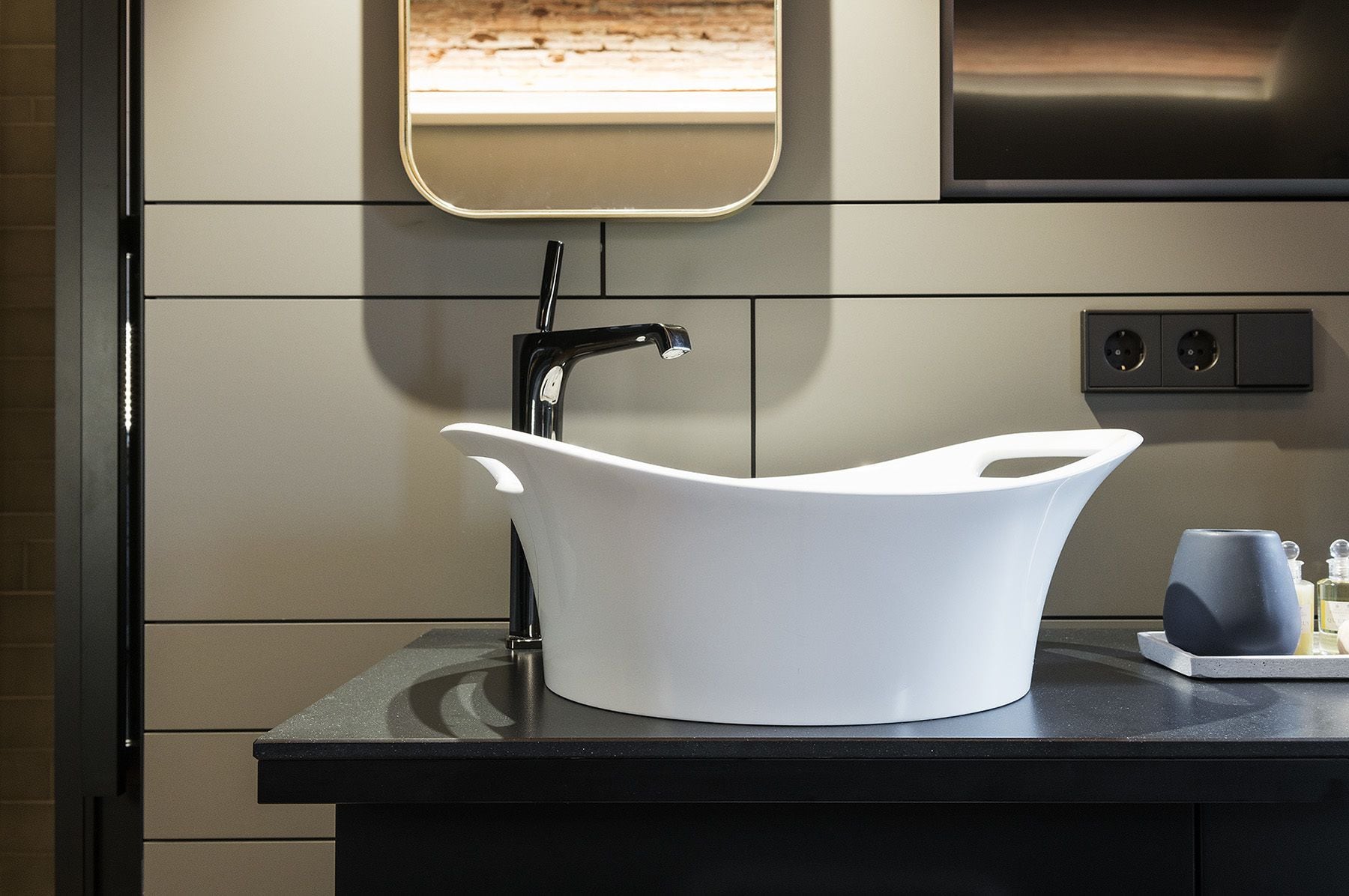 Un baño moderno con un lavamanos blanco, un espejo y una encimera negra.
