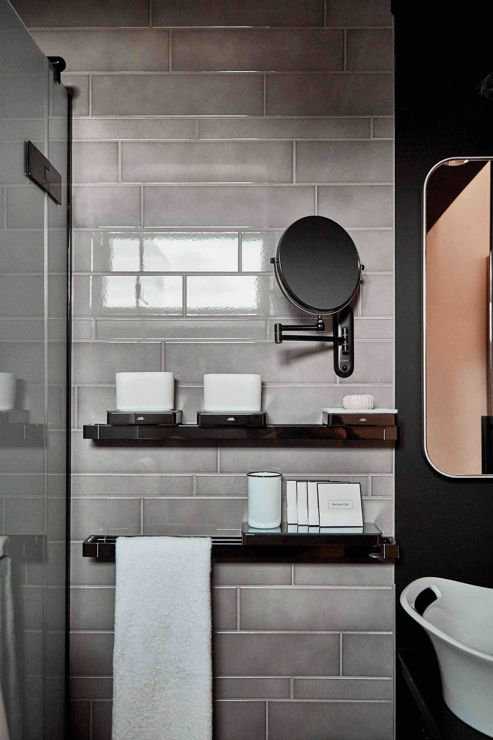 A modern bathroom with grey tiled walls, a black-framed mirror, and white fixtures.