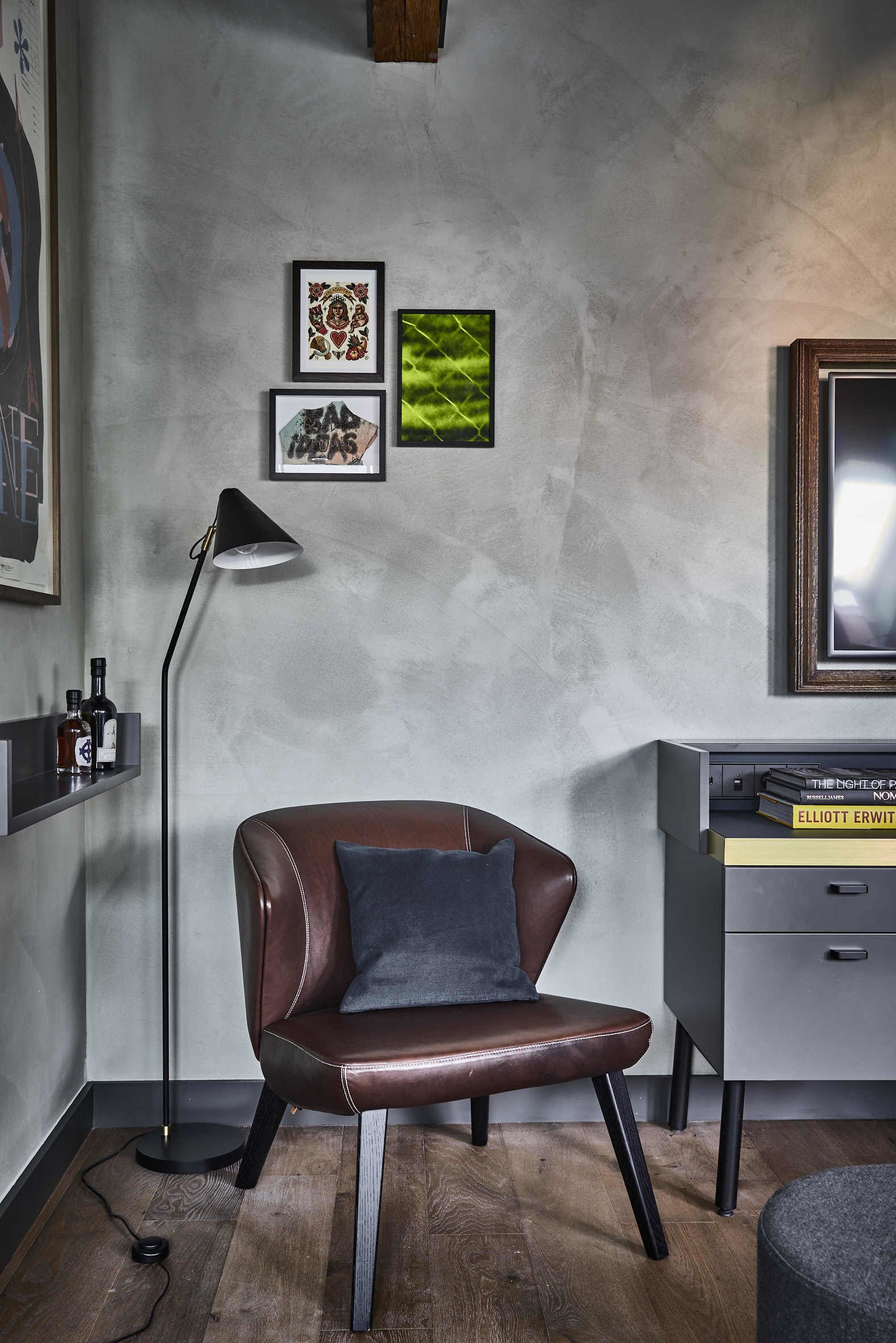 A modern room with a leather chair, a floor lamp, and a desk with books.