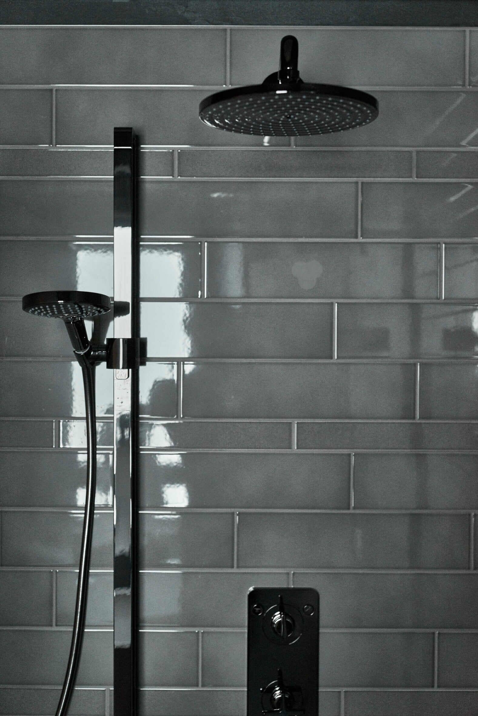 A modern shower with a handheld showerhead and a fixed overhead showerhead, mounted on a tiled wall.
