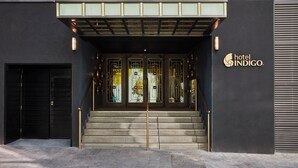 Ein Hotelzugang mit modernem Design, mit einer Treppe, die zu einer Glastür mit dekorativem Metallrahmen führt.