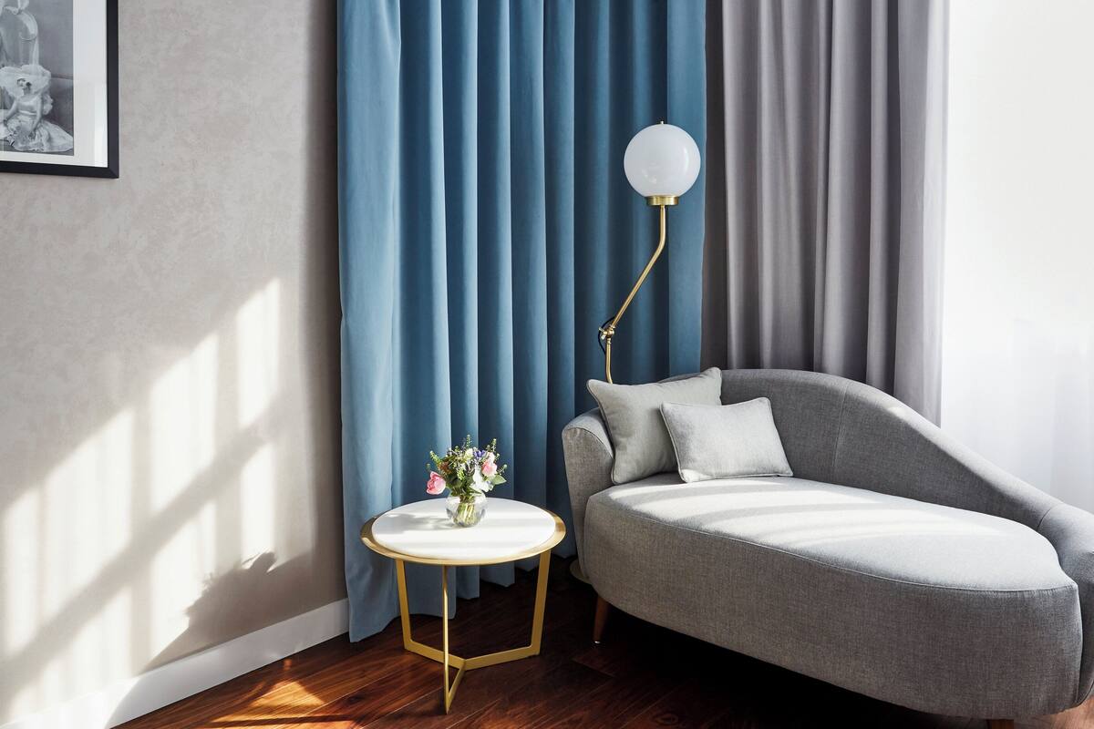 Un salon moderne avec un canapé gris, une table ronde blanche ornée d’un vase de fleurs et un lampadaire.