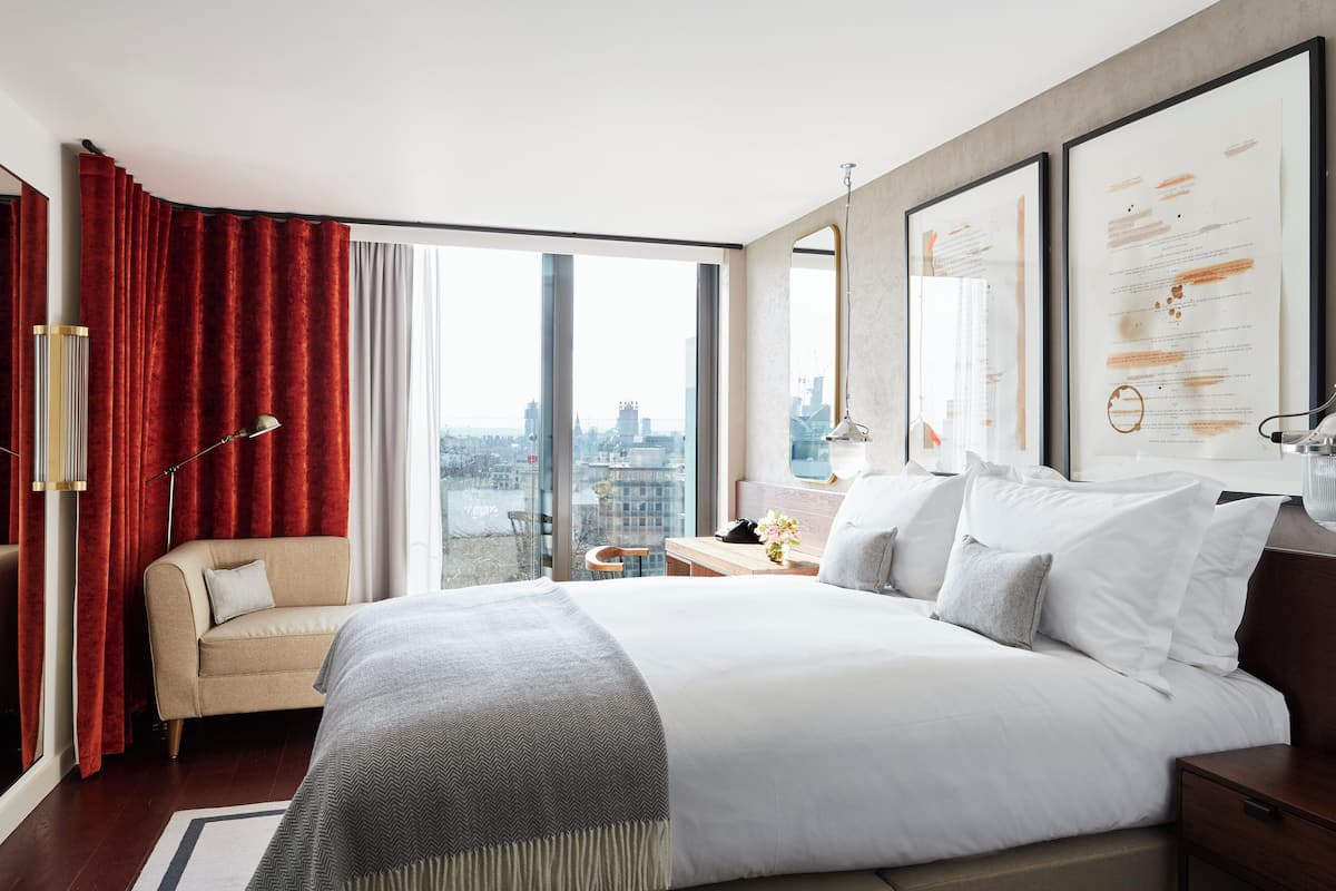 Une chambre d’hôtel moderne dotée d’un grand lit, d’un canapé, d’un bureau et offrant une vue sur la ville grâce à de grandes fenêtres.
