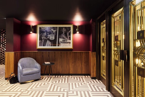 Una habitación con piso estampado, un sillón azul con diseño, una mesita y una pared decorada con carteles enmarcados.