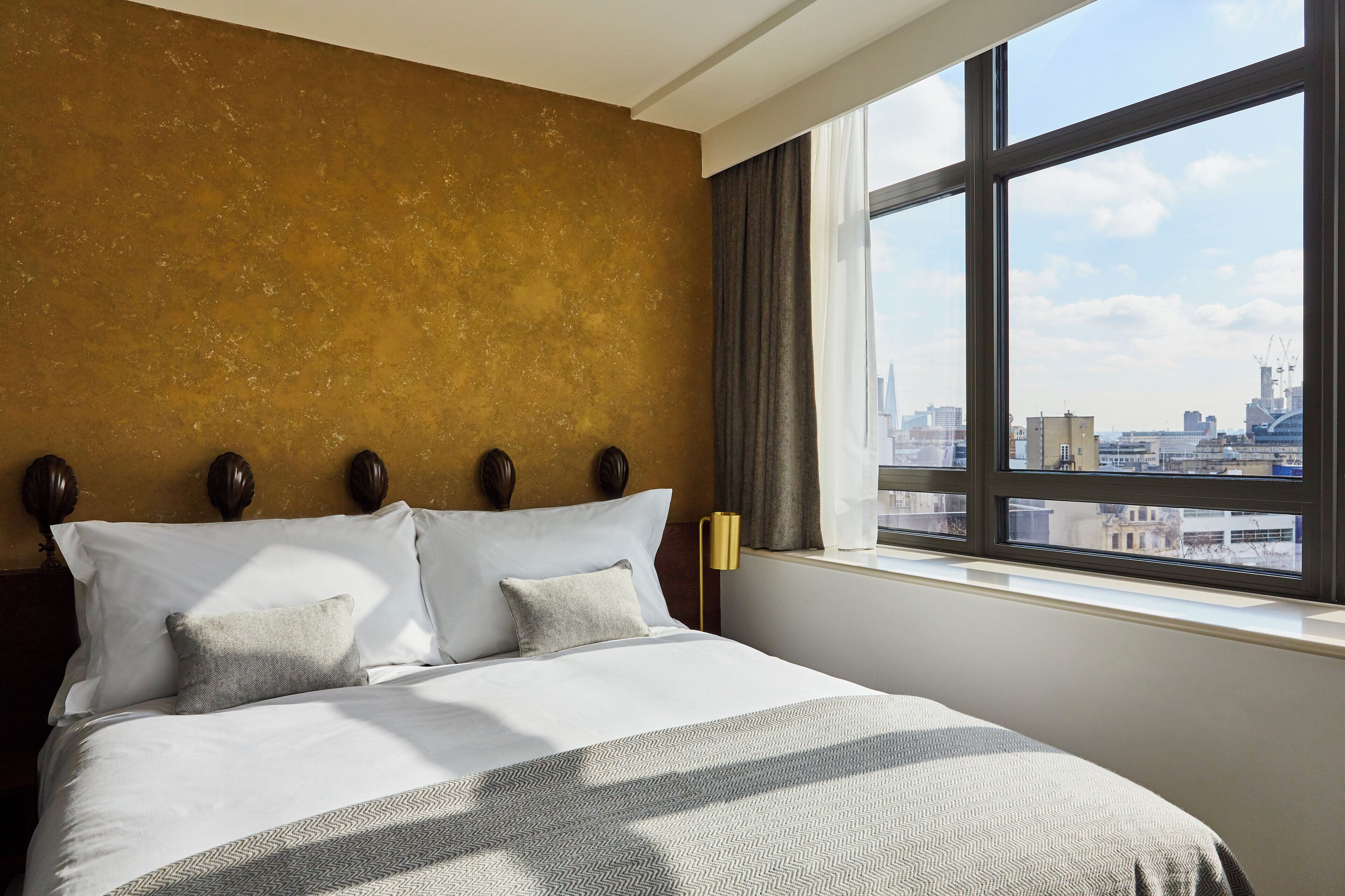 Habitación de hotel con una cama grande, vistas de la ciudad a través de una ventana y una pared con textura.
