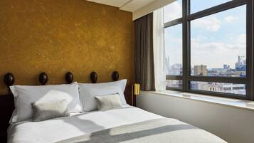 Habitación de hotel con una cama grande, vistas de la ciudad a través de una ventana y una pared con textura.