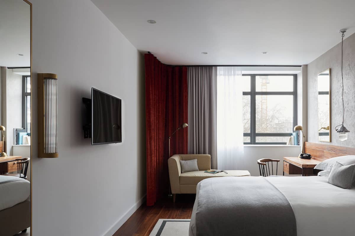 Une chambre d’hôtel moderne avec un grand lit, un bureau, une chaise, un téléviseur fixé au mur et une fenêtre avec des rideaux.