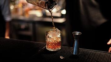 A cocktail being poured into a glass with ice cubes.