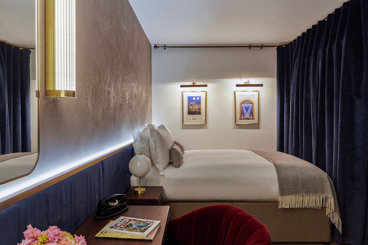 Une chambre d’hôtel avec un lit, une table de chevet, une lampe et des tableaux encadrés au mur.
