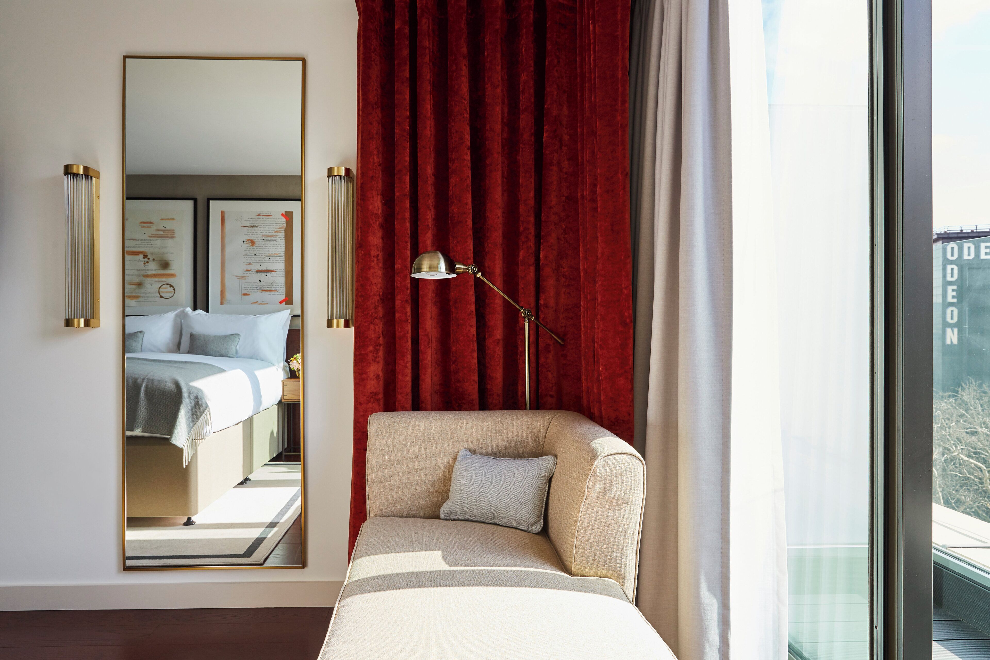 A hotel room with a large mirror, a sofa, a lamp, and a view of the city.