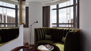 Eine Sitzecke mit grüner Polstersofa, einem kleinen runden Tisch mit Glas und weißem Tuch sowie einer Stehlampe.