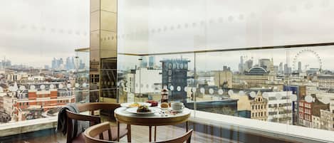 A dining area with a table and chairs, a city view through a large window, and a building with 'ODEON' written on it.