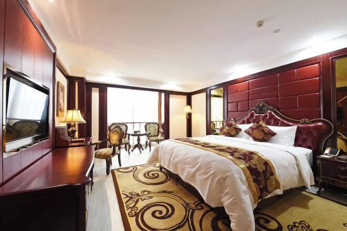 A hotel room with a large bed, a TV, a desk, and a chair.