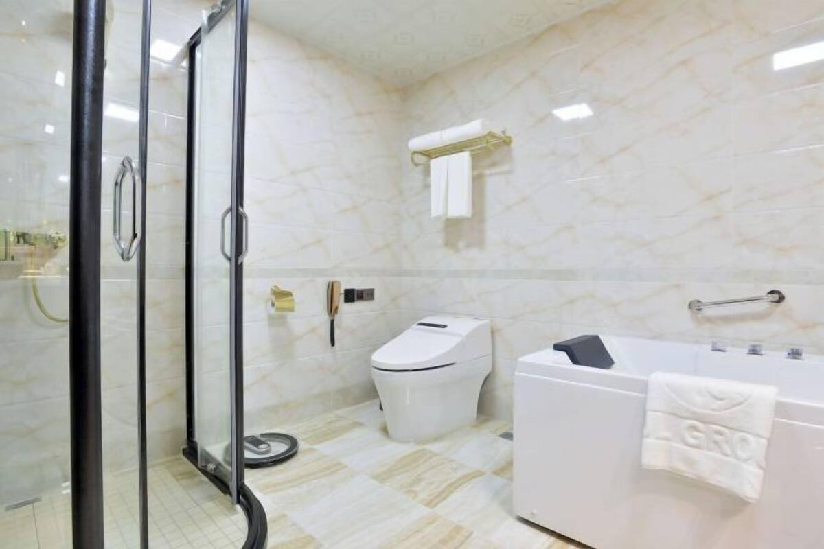 Une salle de bain avec une douche à parois de verre, des toilettes blanches, une baignoire avec une serviette et un sol en marbre.