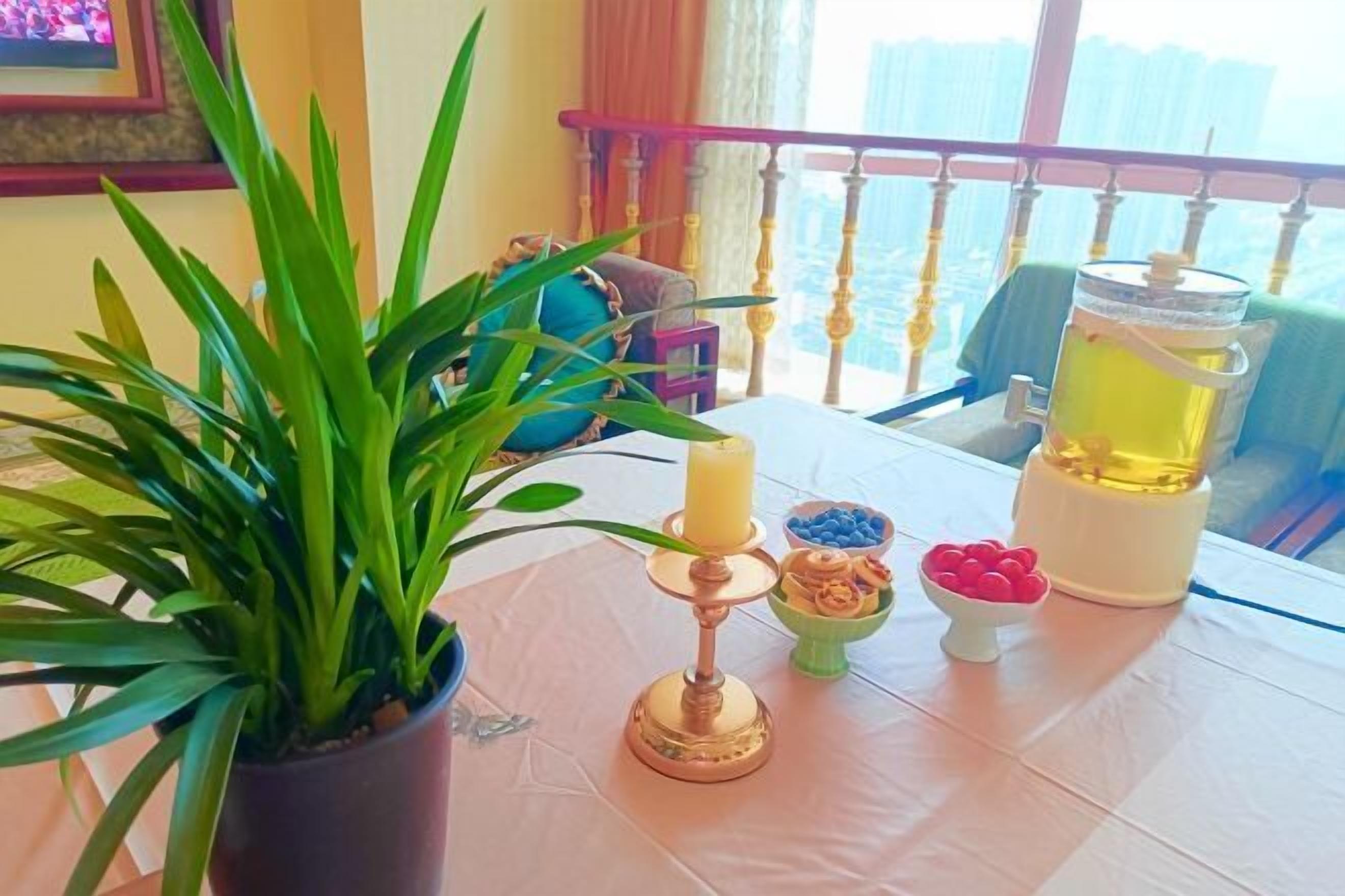 A table with a potted plant, a candle holder, a pitcher of yellow liquid, and a small bowl of red items.