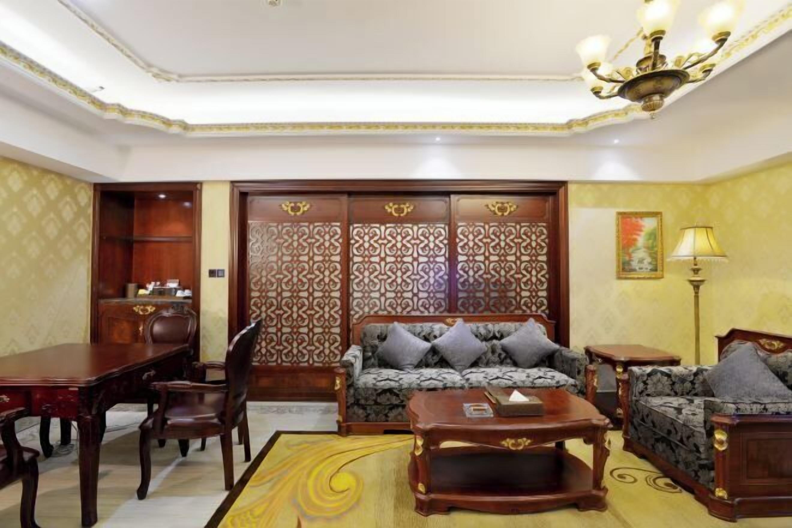 A room with a sofa, a dining table, chairs, a patterned rug, a lamp, and a decorative wall panel.
