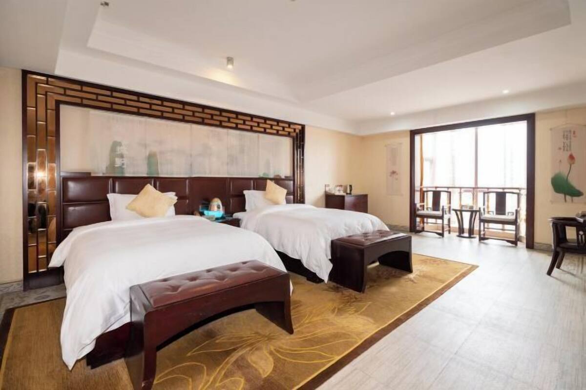 A hotel room with two beds, a large window, a balcony, and a wooden floor.