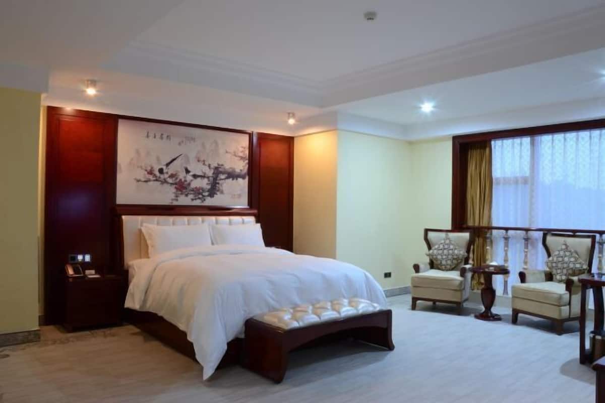 A hotel room with a large bed, a nightstand, a chair, a small table, and a window with curtains.