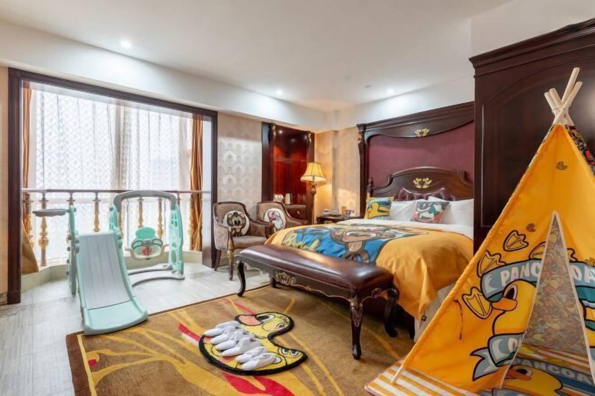 A hotel room with a bed, a bench, a play area, and a window with curtains.