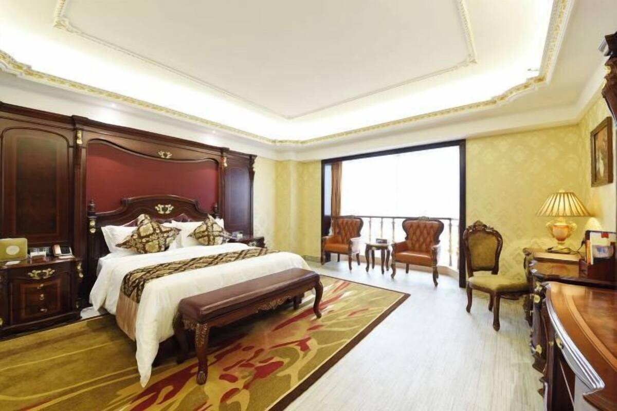 A hotel room with a large bed, a bench, a desk, a chair, and a balcony with a view.