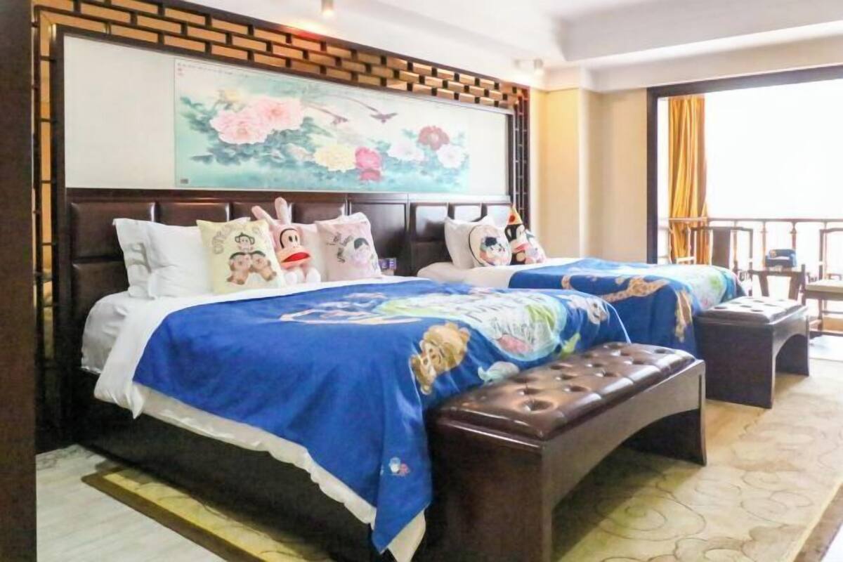 A hotel room with two beds, a large painting on the wall, a balcony with a view, and a wooden headboard.