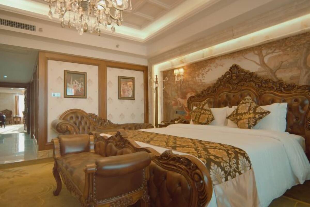 A luxurious bedroom with a large bed, ornate headboard, and a chandelier.