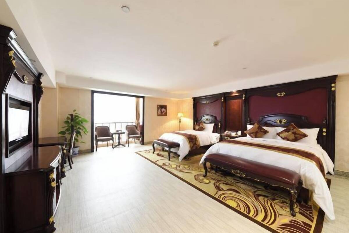 A hotel room with a large bed, a desk, a chair, a TV, and a view of the outside.