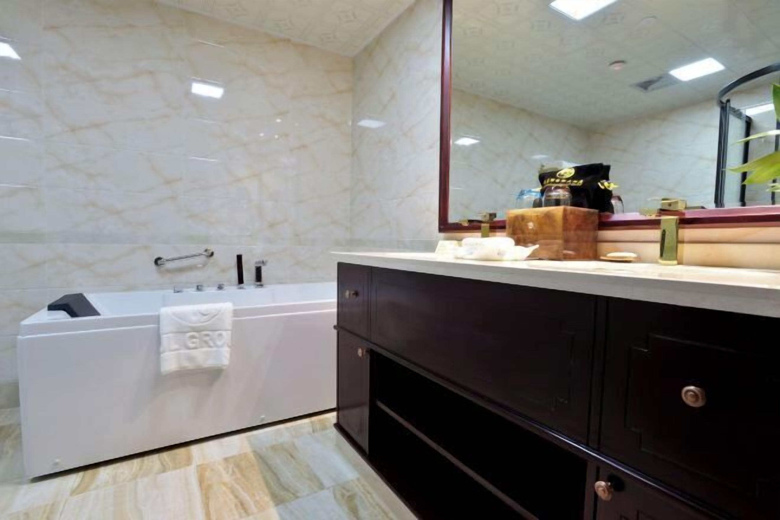 A modern bathroom with a marble wall, a large mirror, a bathtub, and dark-toned cabinets.