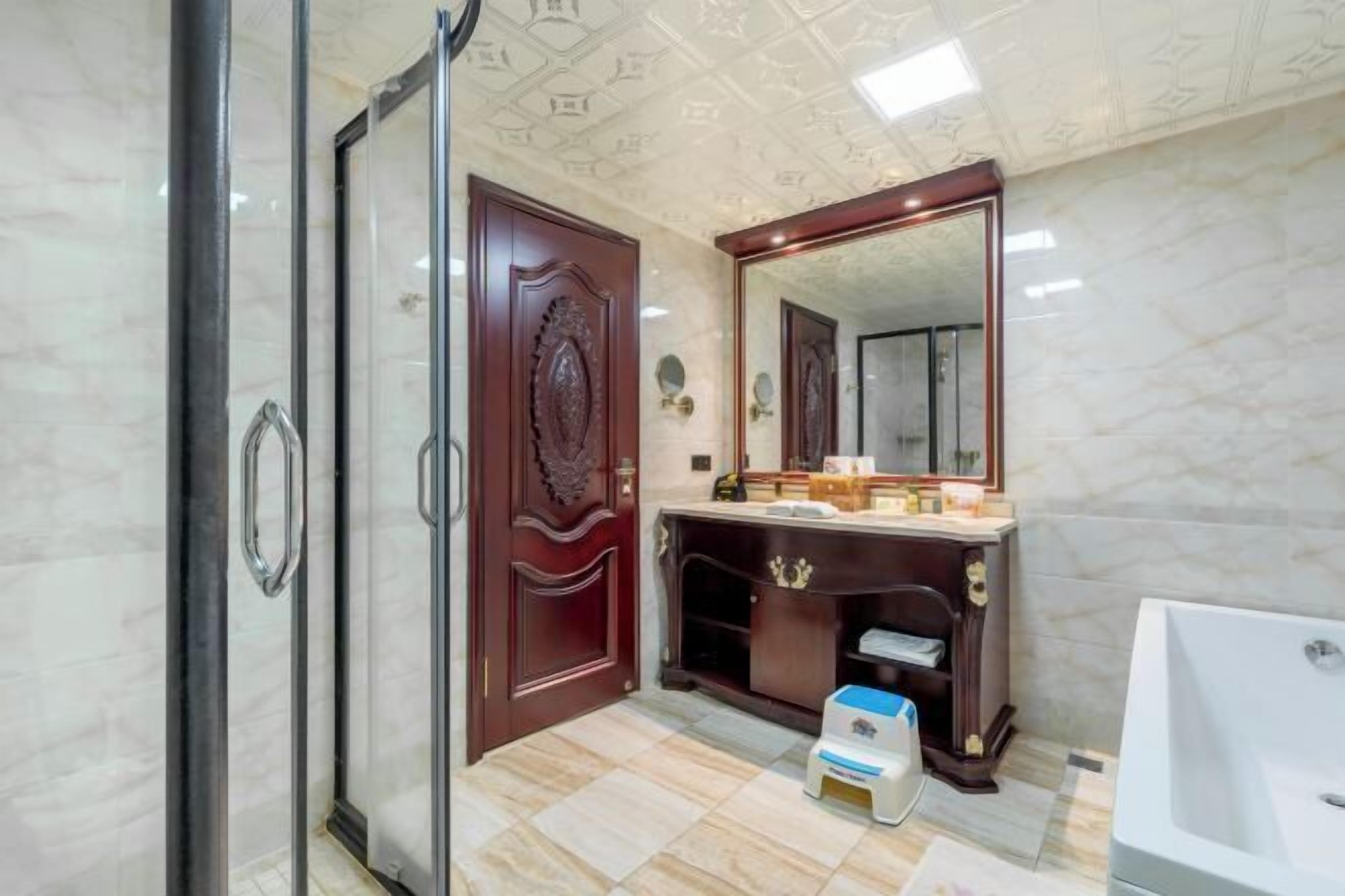 A bathroom with a marble floor, a wooden vanity, a large mirror, and a bathtub.