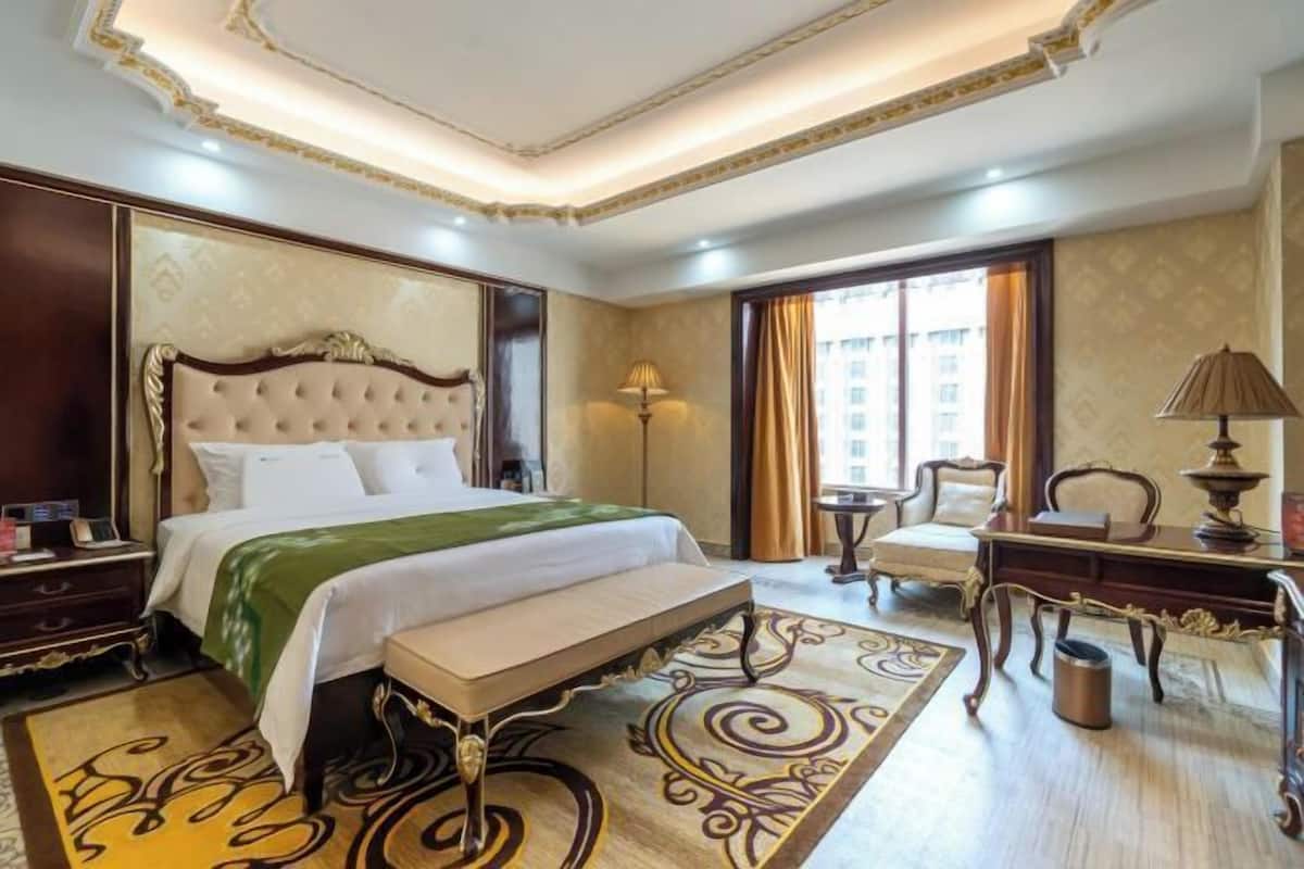 A hotel room with a large bed, a desk, a chair, and a view of the city.