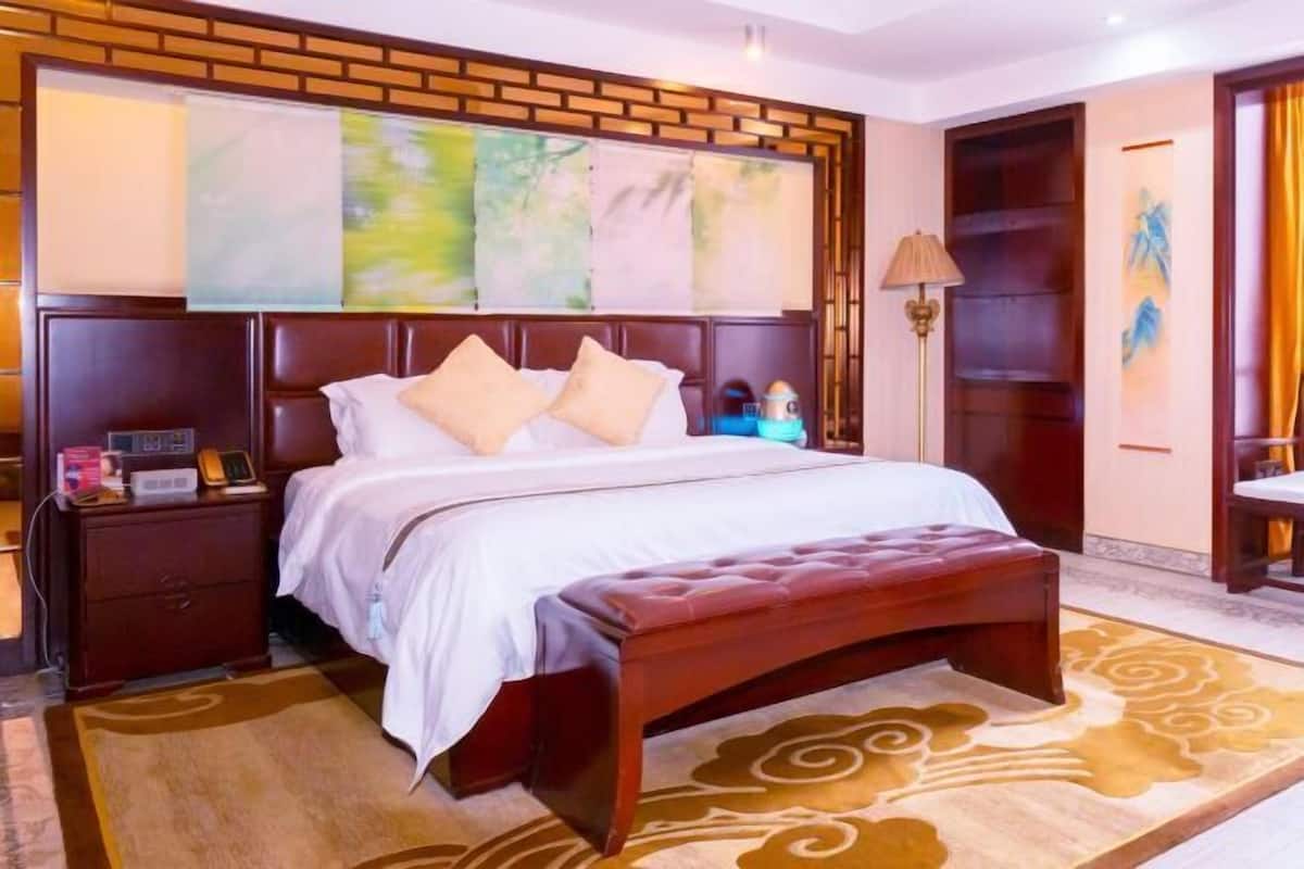 A bedroom with a large bed, a wooden headboard, a bedside table, a lamp, and a wall-mounted artwork.