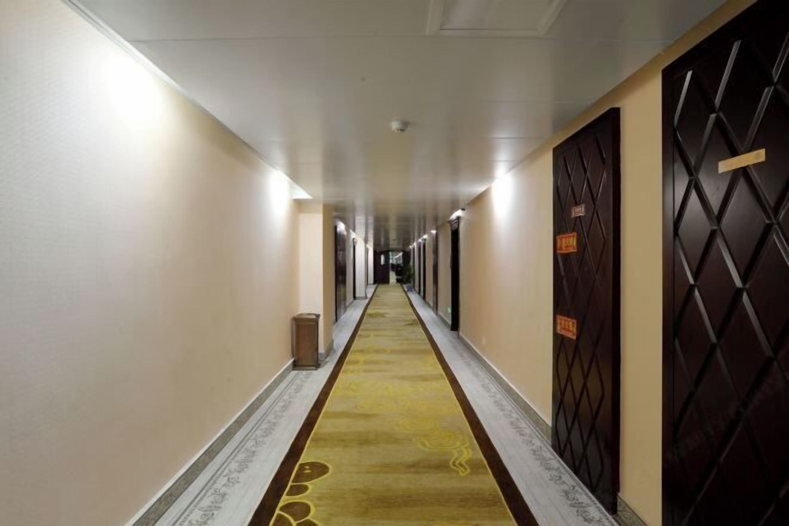 Et hotel med møbelklædt gangareal, døre på begge sider og loftlamper.