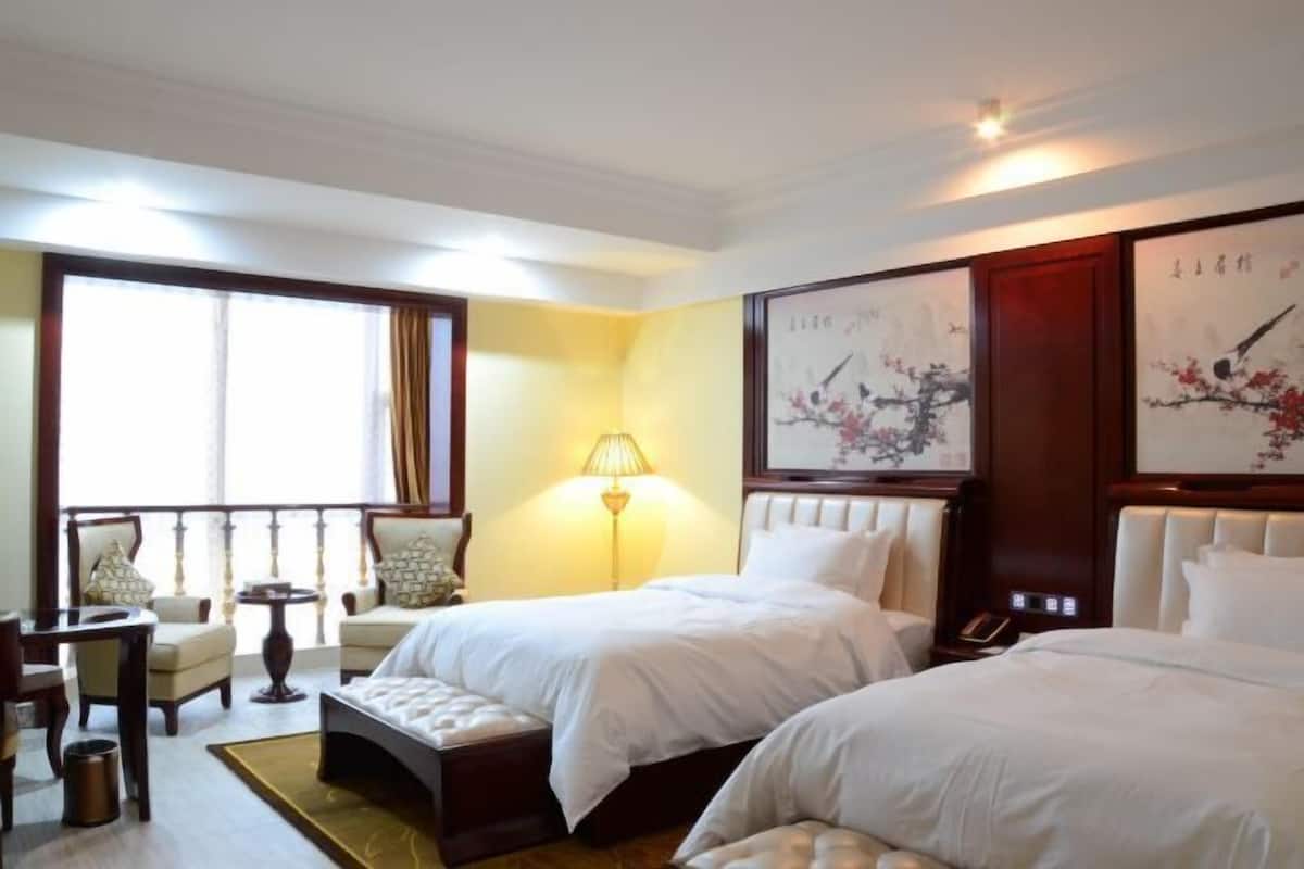 A hotel room with two beds, a sitting area with chairs, a lamp, and artwork on the walls.