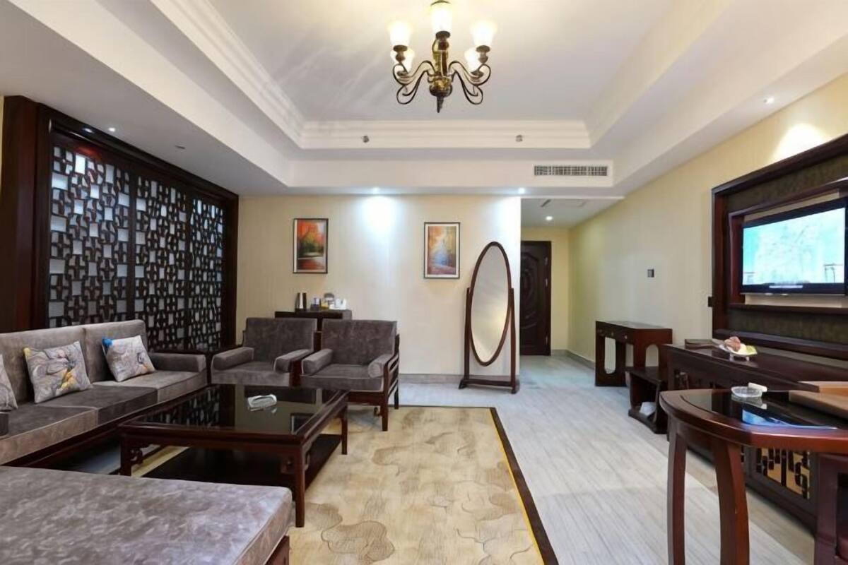 A spacious living room with a sofa set, armchairs, a coffee table, a TV, and a decorative wall.
